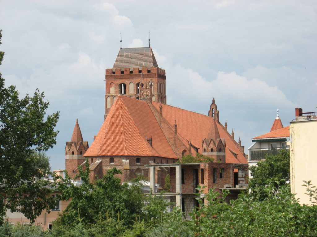 Red-brick cathedral with orange-red roof surrounded by trees