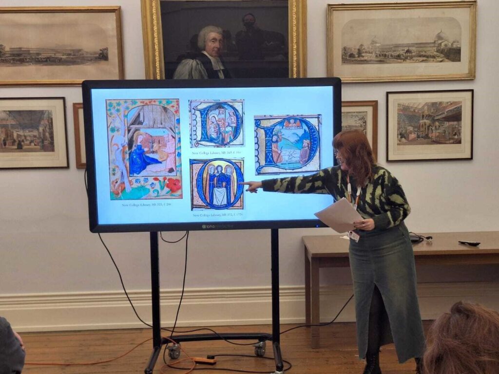 New College's Curatorial Assistant gives a talk, pointing to a manuscript illumination of the Holy Family on a screen.