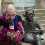 Philip Flacke sitting on a bench reading a pamphlet next to a statue of Lichtenberg